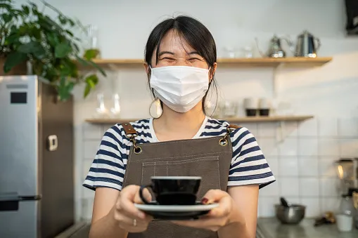 Barista in a striped top and apron holding out a freshly made coffee on a saucer