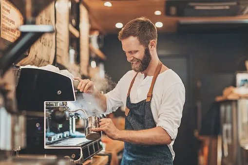 Barista steaming milk at a professional espresso machine behind a café counter