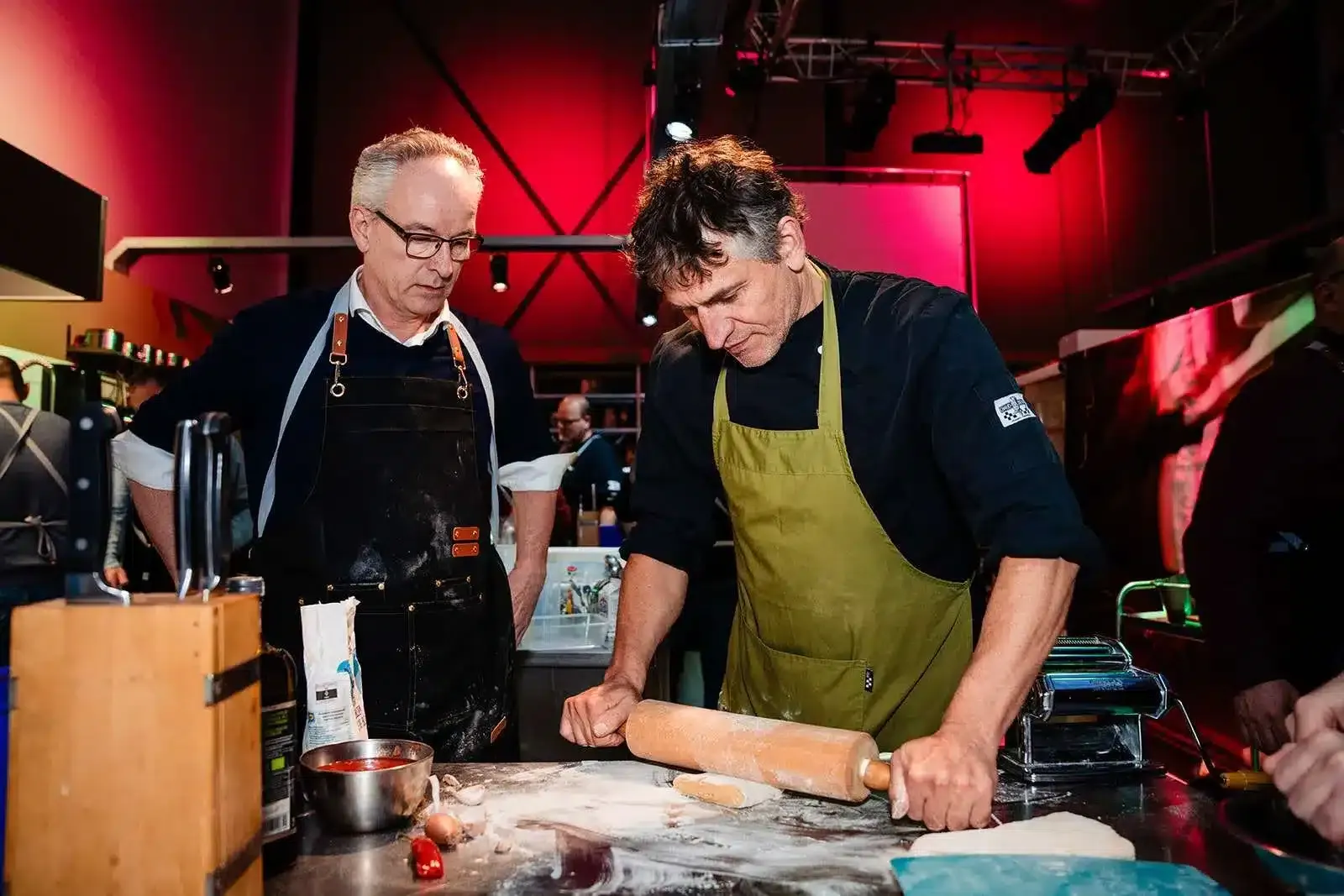 Två kockar i förkläden kavlar ut deg i ett professionellt kök