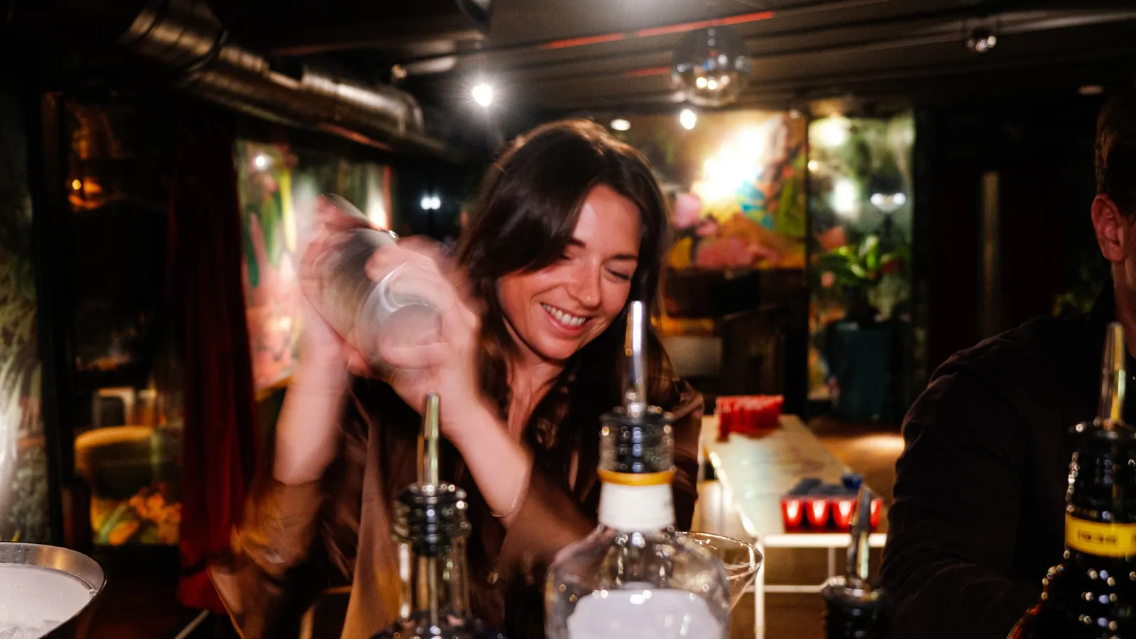 Smiling guest shaking a cocktail at a dimly lit bar