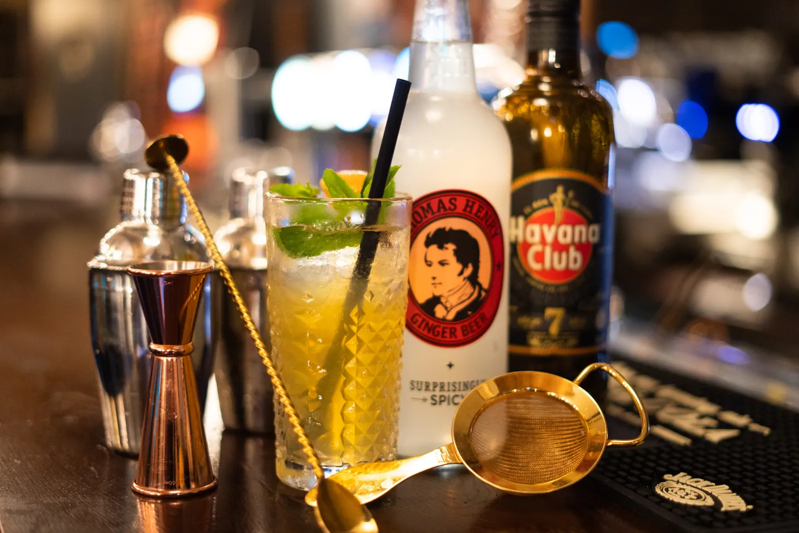 Mint-topped cocktail beside a shaker, jigger and strainer on the bar