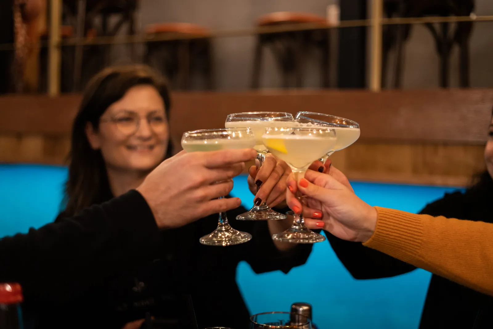 Guests raising coupe glasses of freshly mixed cocktails in a toast