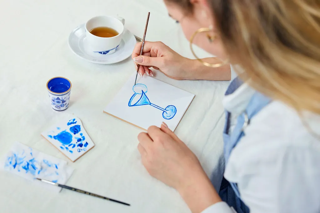 Ospite che dipinge un bicchiere da cocktail blu su una piastrella accanto a una tazza di tè