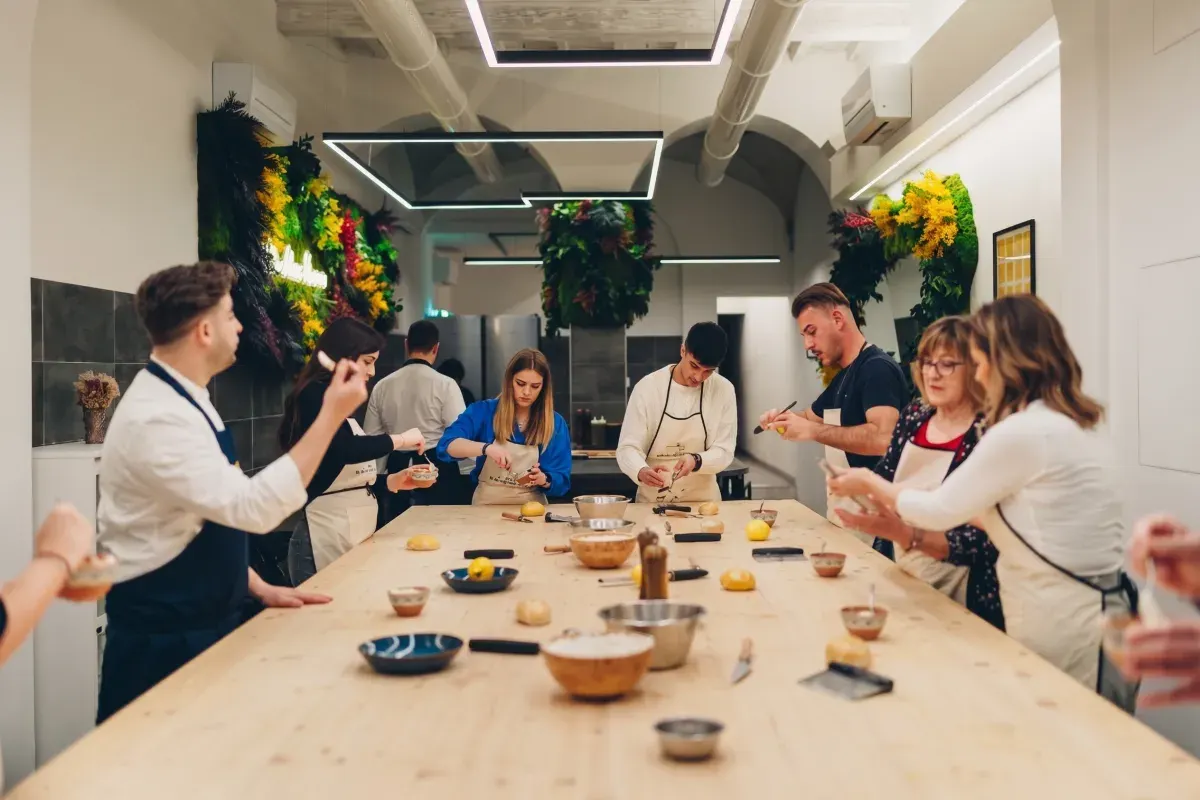 Guests in aprons shaping fresh dough at a long wooden table in a bright cooking studio