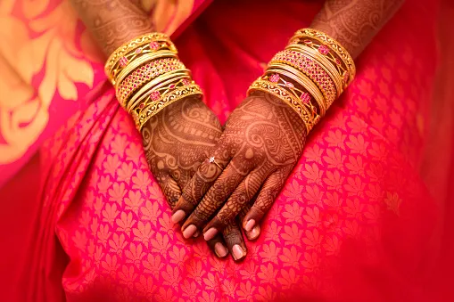 Hands with detailed henna patterns and gold bangles resting on pink silk