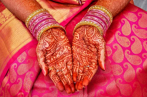 Open palms covered in fine henna designs above a pink and gold fabric