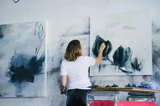 Artist painting large dark flower shapes on a white canvas