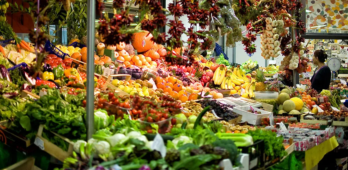 Colourful market stall piled high with fresh vegetables and fruit under hanging dried peppers