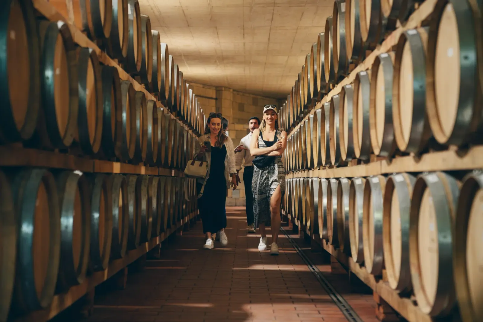 Visitors walking down a long cellar lined on both sides with large wooden wine barrels