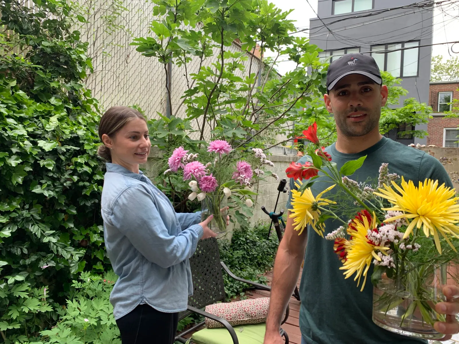 Two guests smiling in a garden, one holding a bunch of pink flowers and the other a bold yellow and red bouquet