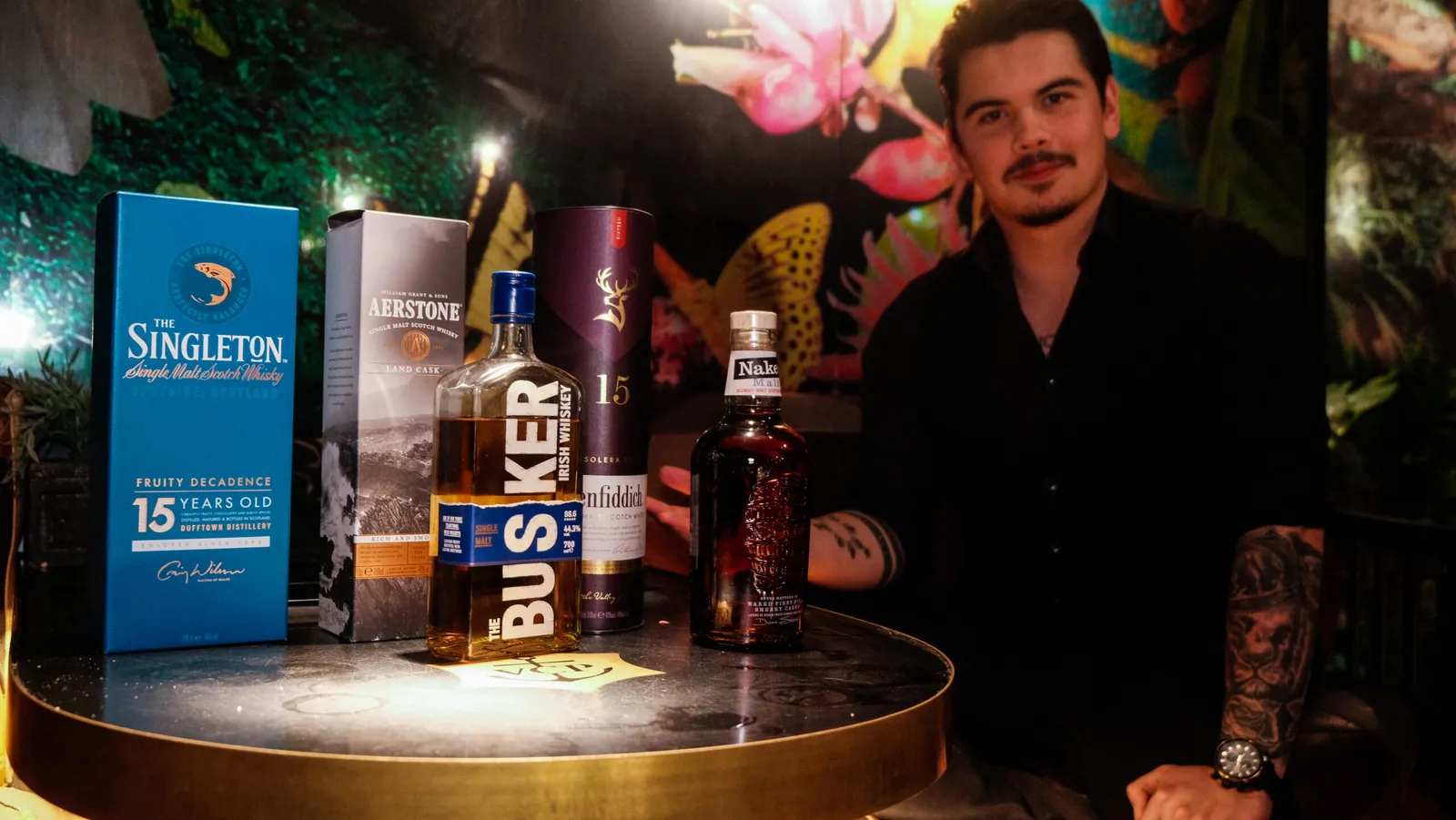 Vært sidder bag et rundt bord med flasker single malt