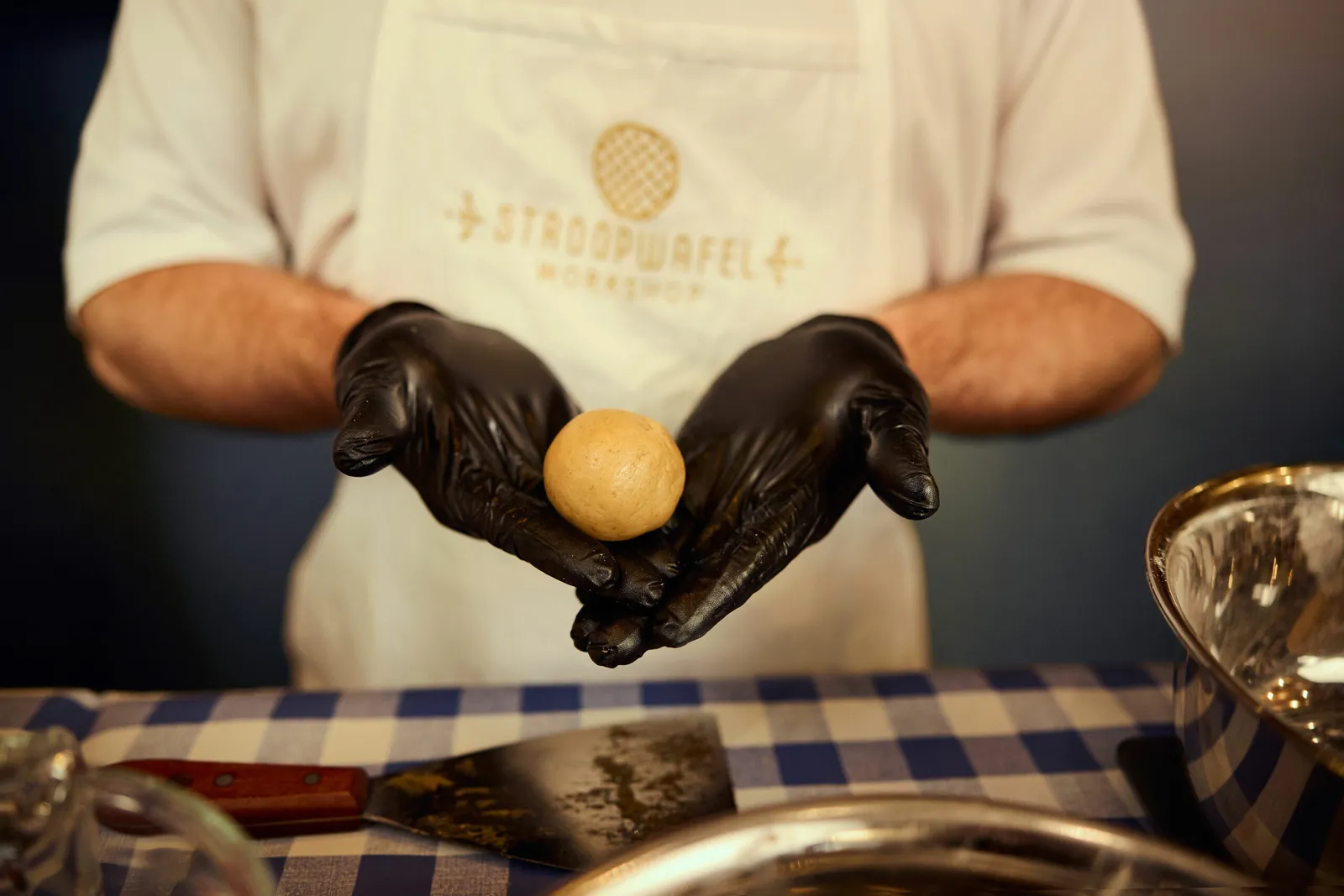 Gloved hands holding a ball of stroopwafel dough, ready for the iron