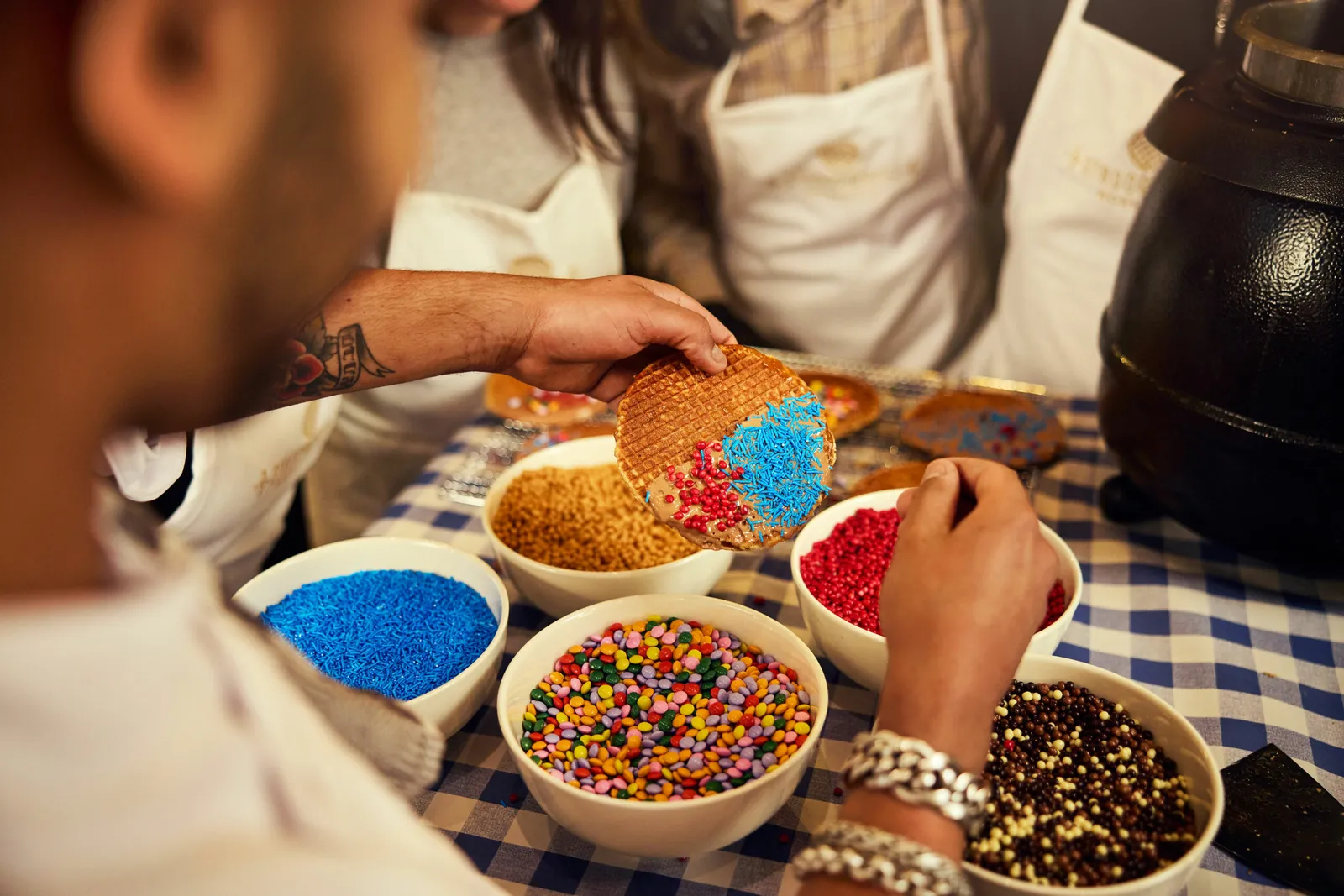 Dipping the edge of a syrup-filled stroopwafel into bowls of colourful sprinkles