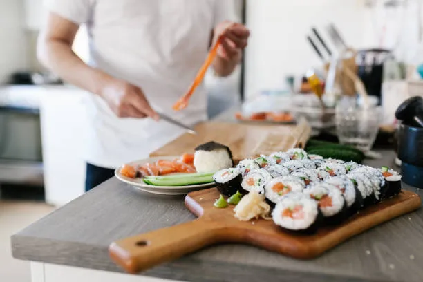 Freshly sliced maki rolls on a wooden board while a cook slices more