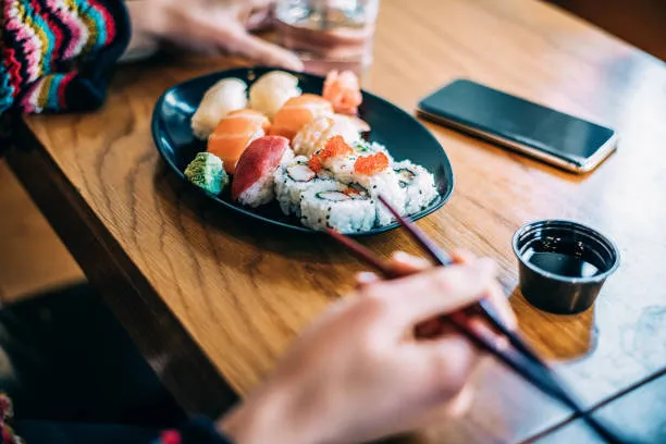Plate of nigiri and maki being shared with chopsticks, beside a dish of soy sauce